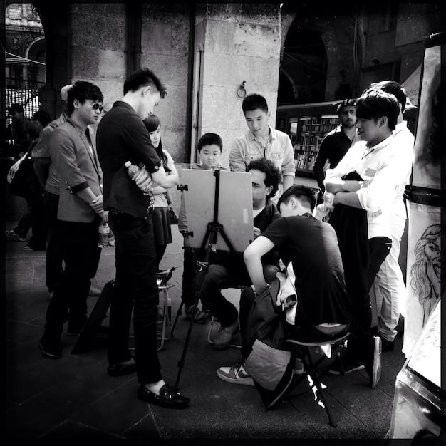 A candid shot of Jaehyun on a film set during a break. He is surrounded by crew members, and there are cameras in the background. The image conveys a sense of focused preparation and collaboration.