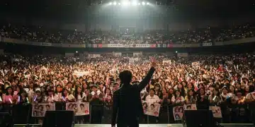 Excited dorama fans at a large fan meetup event in a US arena, holding lightsticks and banners.