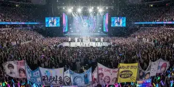 K-Pop fans holding lightsticks and banners at a concert in a U.S. city.